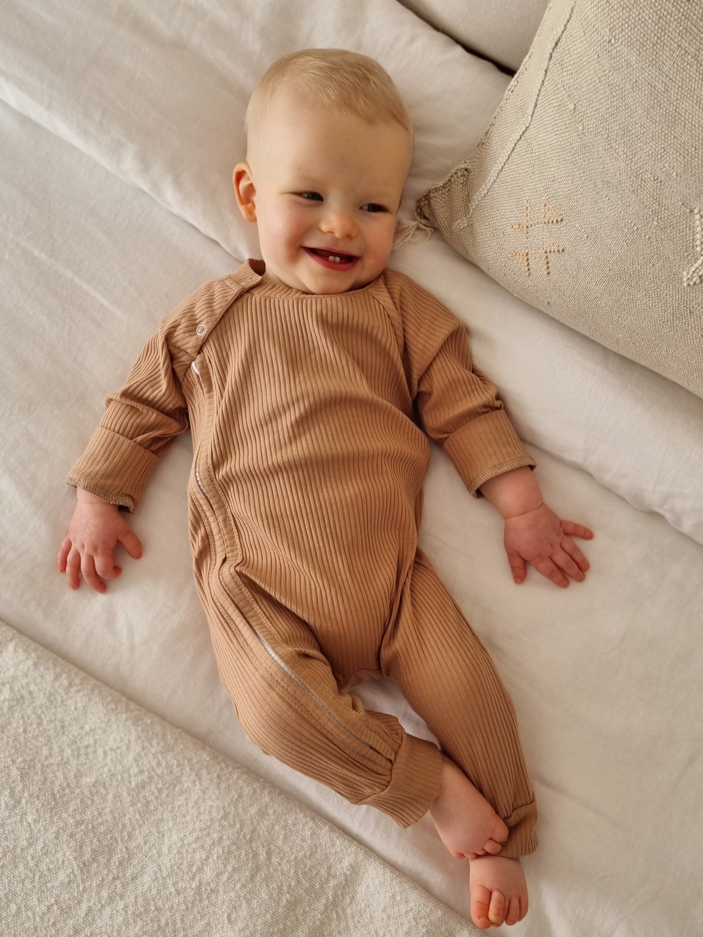 Baby wearing a ribbed fabric, zip up jumpsuit in a caramel colour