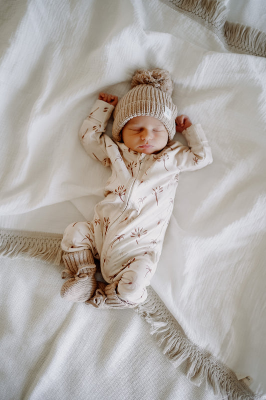 Newborn wearing the winter onesie in the Desert Palm design, paired with beanie & booties (Beanie / booties not included)