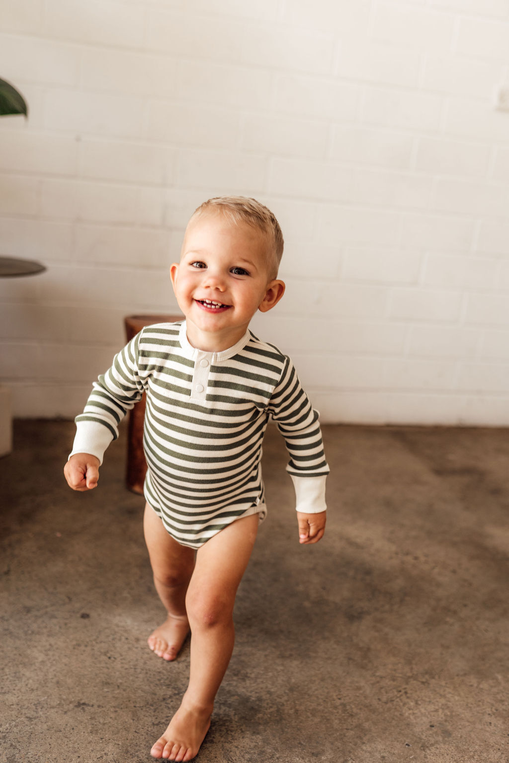 Olive stripe bodysuit with foldable hand mittens worn by a toddler.