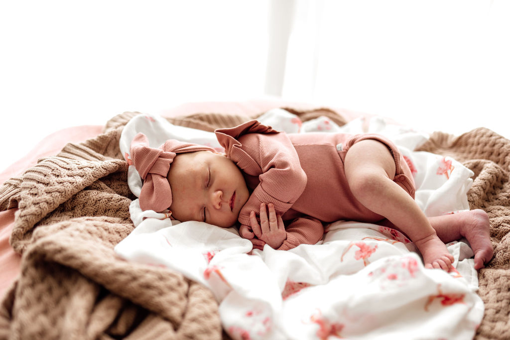 Newborn dressed in the rose pink body suit in organic rib material. It has small frills on the shoulders & 3 button clips in the crutch for easy nappy changes.. has fold over cuffs to keep hands warm & prevent scratches.