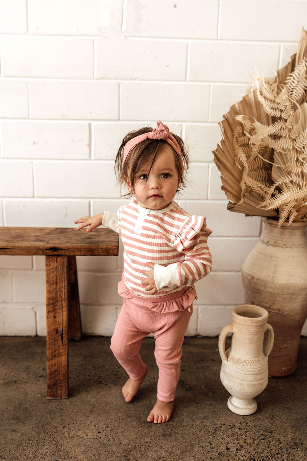 Toddler dressed in the rose stripe bodysuit, paired with rose coloured pants (sold separately)