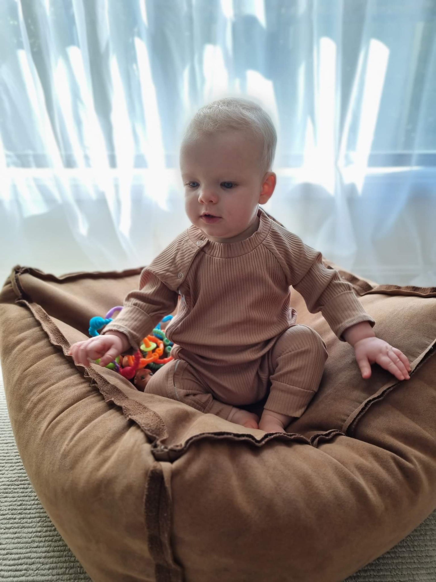 Baby wearing a ribbed fabric, zip up jumpsuit in a caramel colour