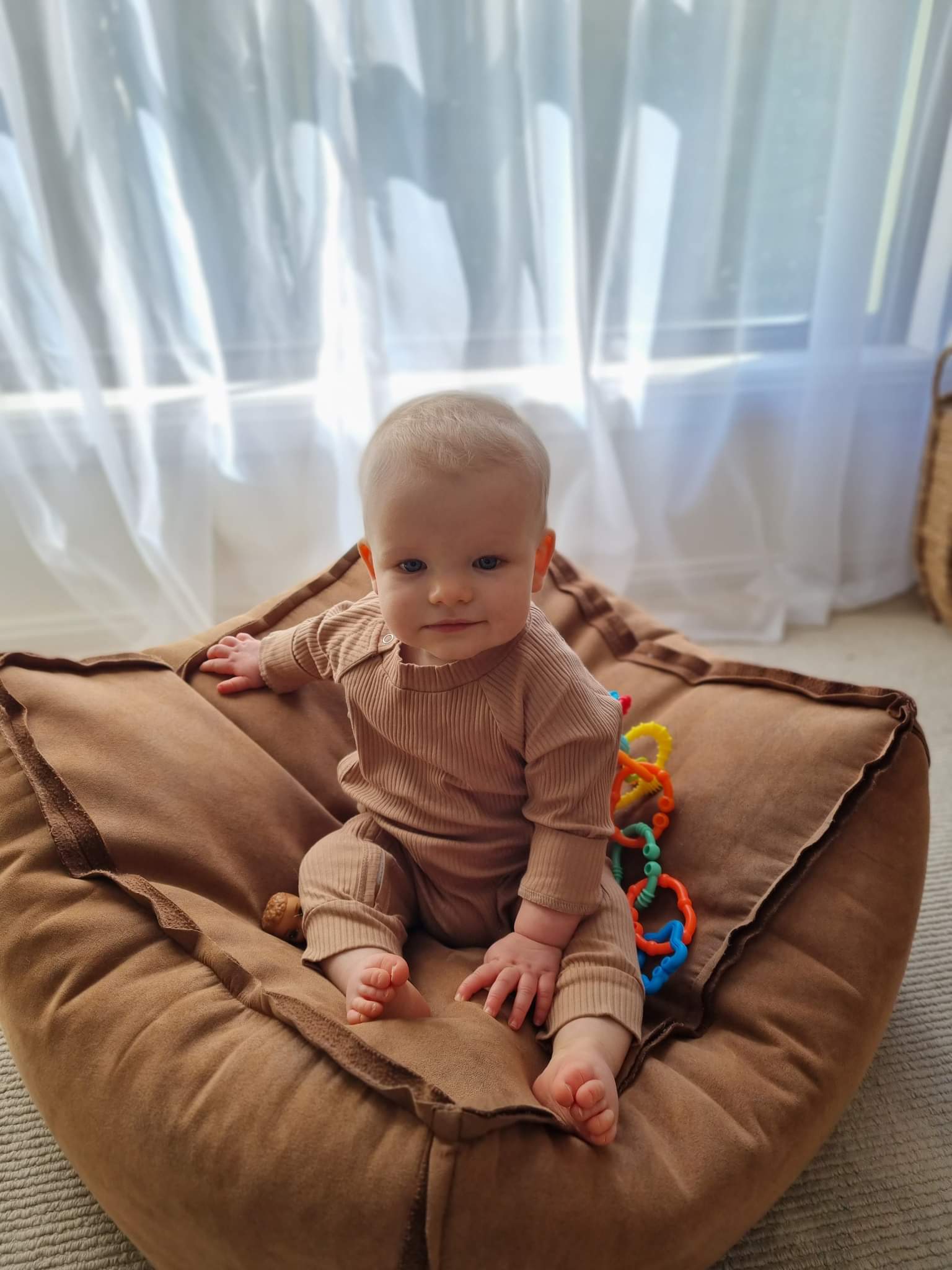 Baby wearing a ribbed fabric, zip up jumpsuit in a caramel colour